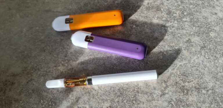 Tre olika HHC vapes ligger bredvid varandra. Två är engångsvapes i orange respektive lila plast. Det andra är en vape cart med glaskapsel och vit batteri