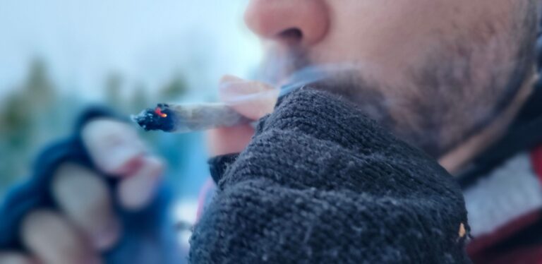 Närbild på en man som röker en joint fylld med THCP buds mot en suddig bakgrund i vintermiljö.