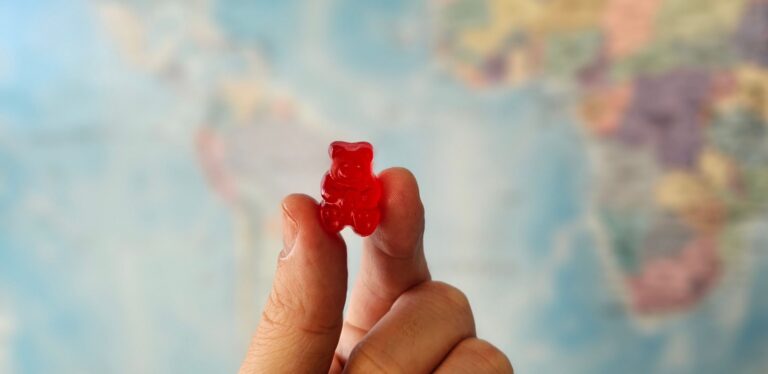 Hand håller en röd HHC gummy framför en världskarta.