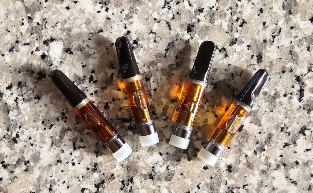 Fyra CBD vape cartridges fyllda med gyllene extrakt på en kontrasterande granitbänkskiva.