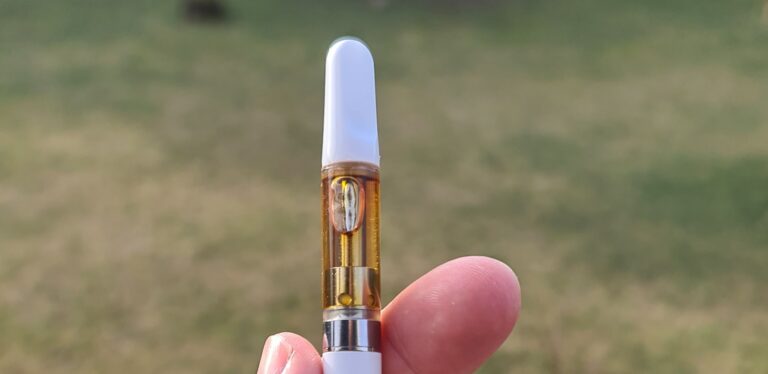 En H4CBD vape cart med vitt munstycke hålls mellan två fingrar.