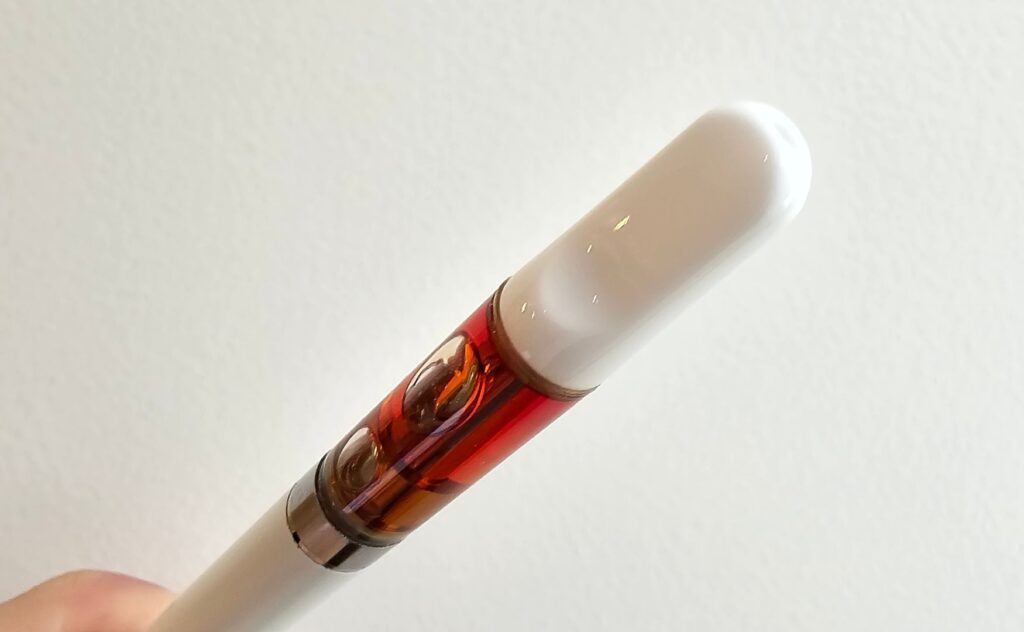 En canntropy HHCPO vape cart hålls upp mot vit bakgrund. Både batteri och munstycke är vitt och konstraterar mot den gyllene vätskan.