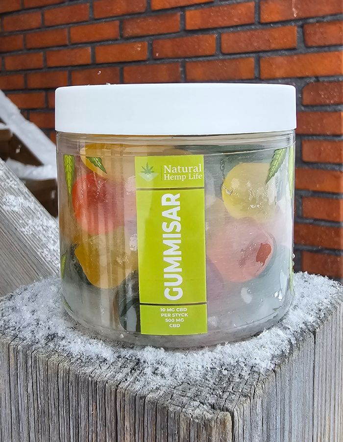 En burk Natural Hemp Life CBD gummies står på en träpåle. I bakgrunden syns en tegelvägg