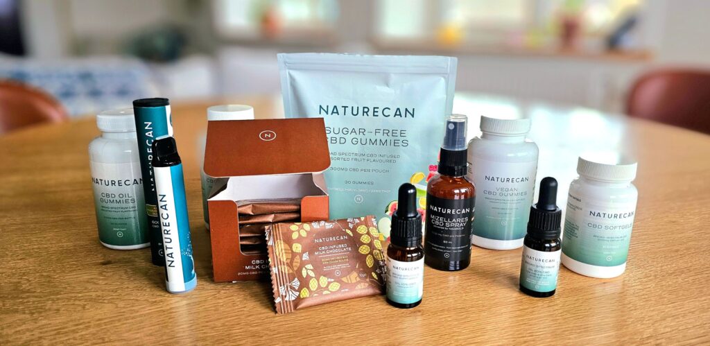 CBD produkter från tillverkaren Naturecan står uppställda på ett träbord.