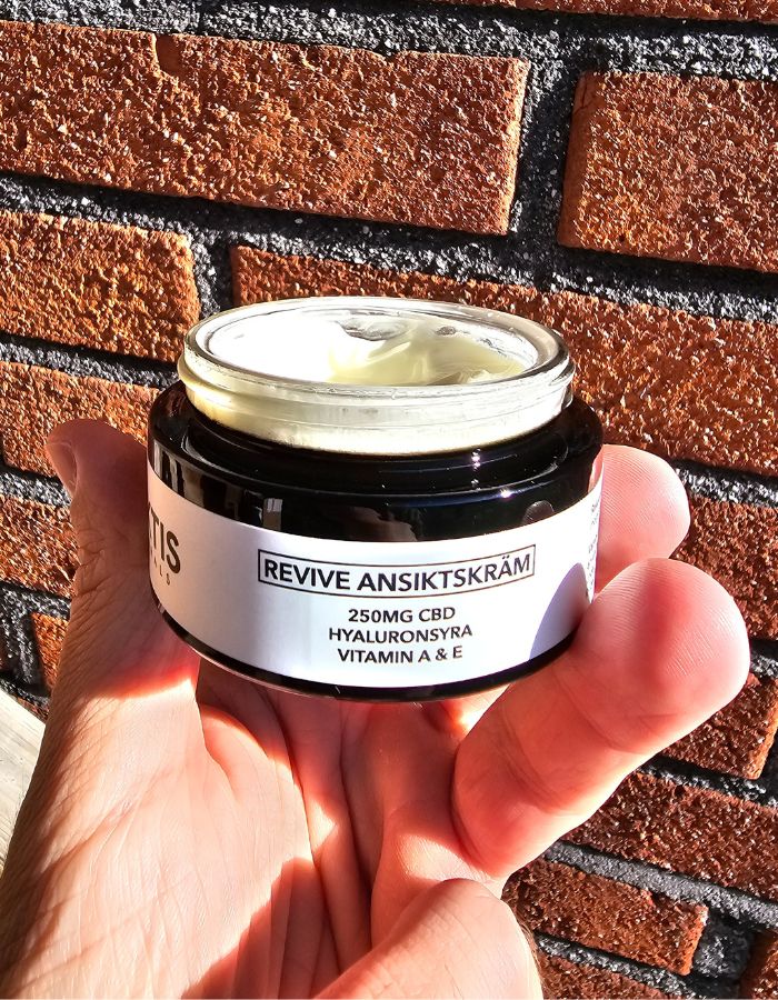 En öppnad burk med CBD Revive ansiktskräm från Arktis Naturals hålls i en hand.